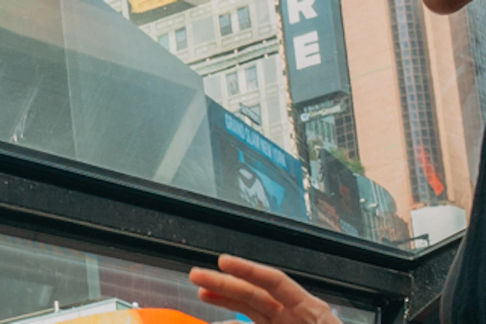 People dining inside a glass-roofed vehicle in an urban area with billboards and skyscrapers visible outside.