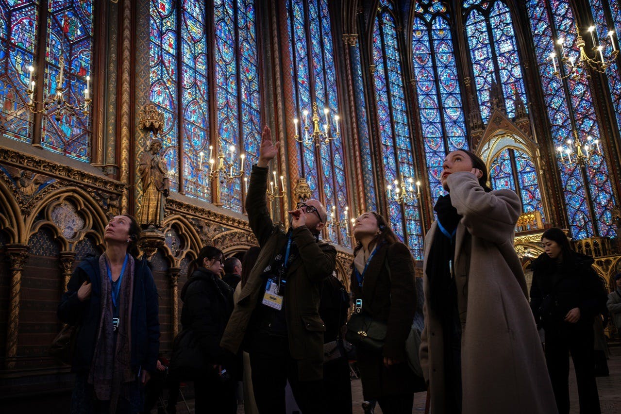 People admiring the intricate stained glass windows and ornate interior of a historic cathedral with tall candlesticks.