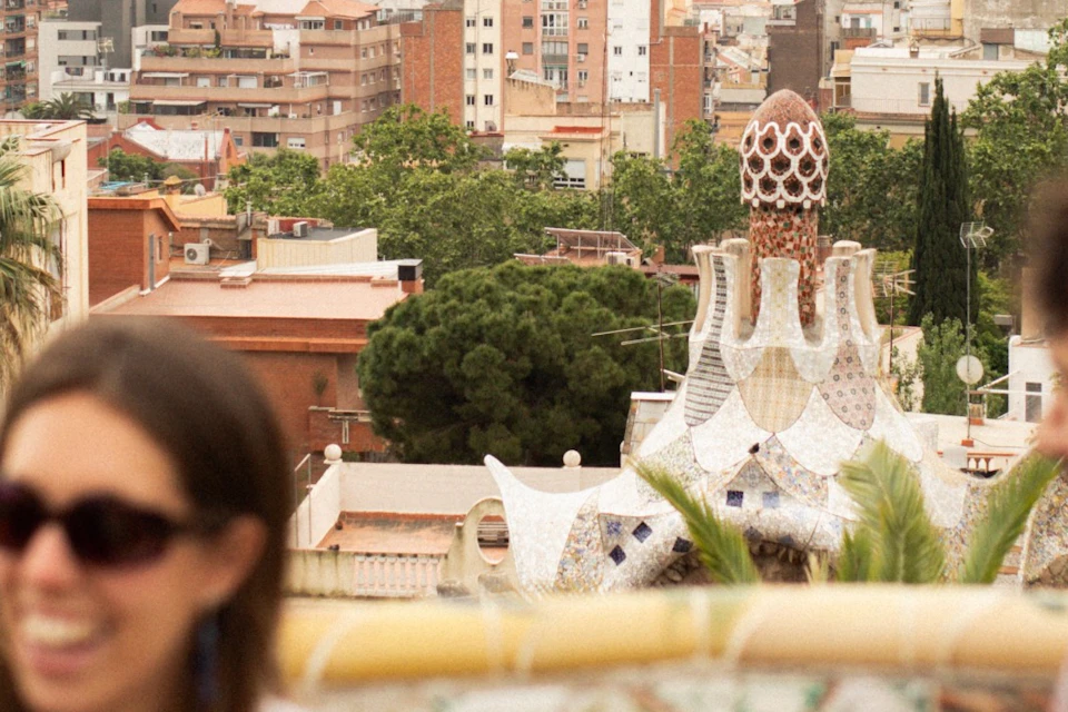 Three people sitting on a mosaic bench overlooking a cityscape with unique architecture and distant skyscrapers.