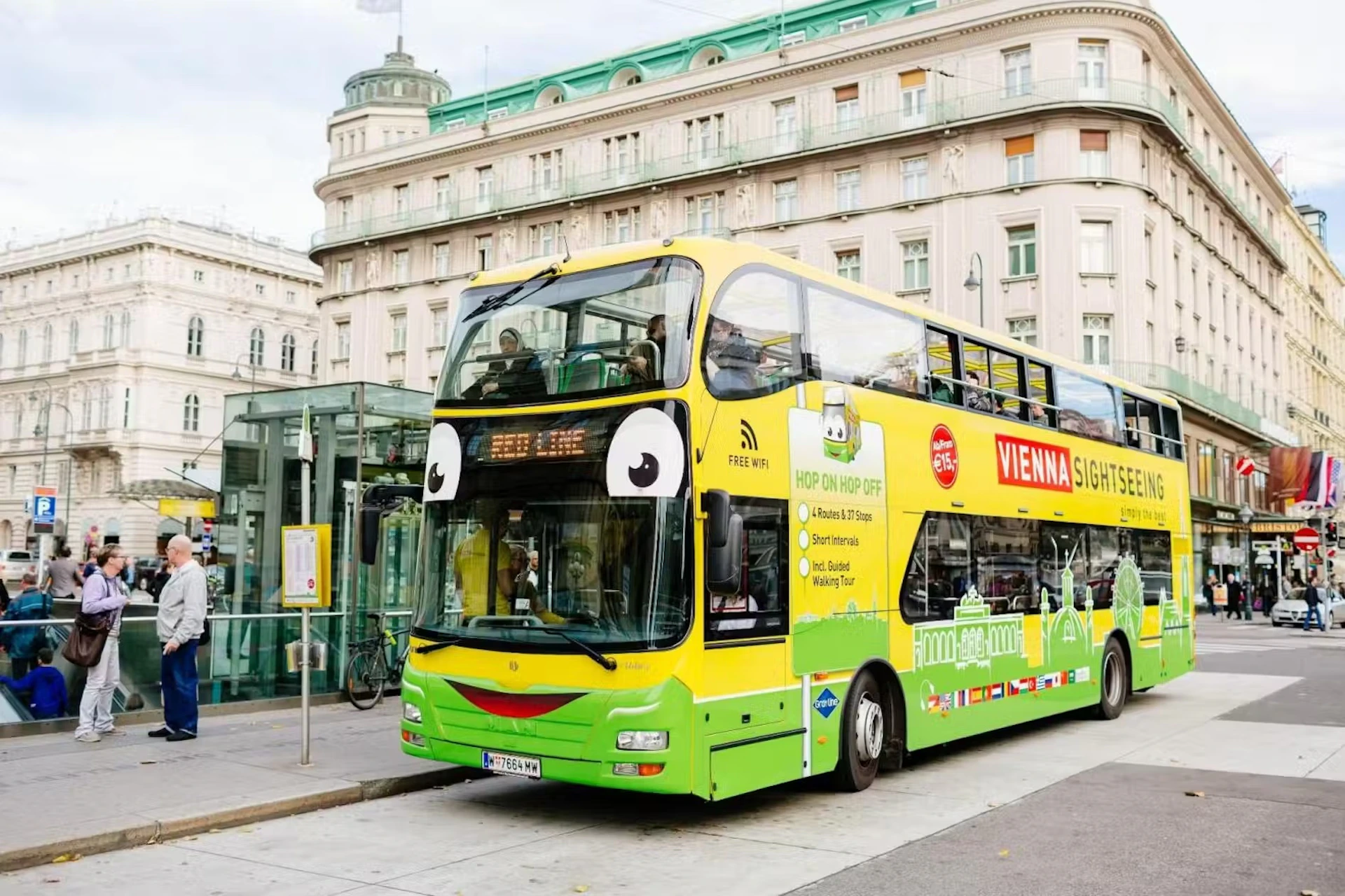 A double-decker sightseeing bus with a cartoon face parked in front of a historic building in Vienna.