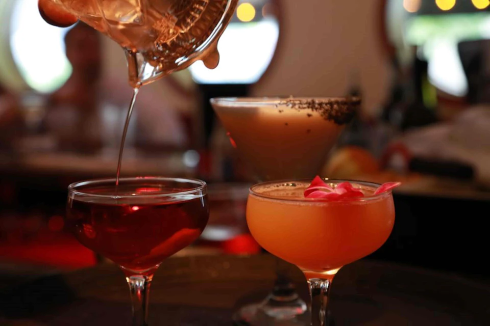 Three cocktails in elegant glasses, with one being poured from a shaker. One cocktail is garnished with a flower.