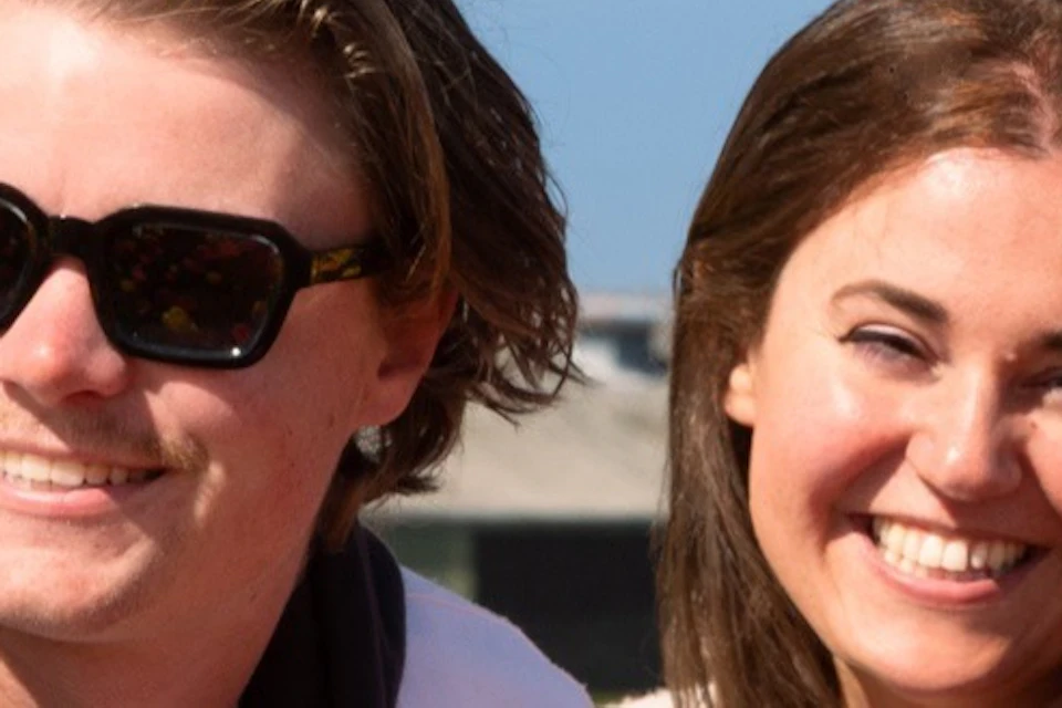 Two people smiling while sitting in a colorful tulip field under a clear blue sky.