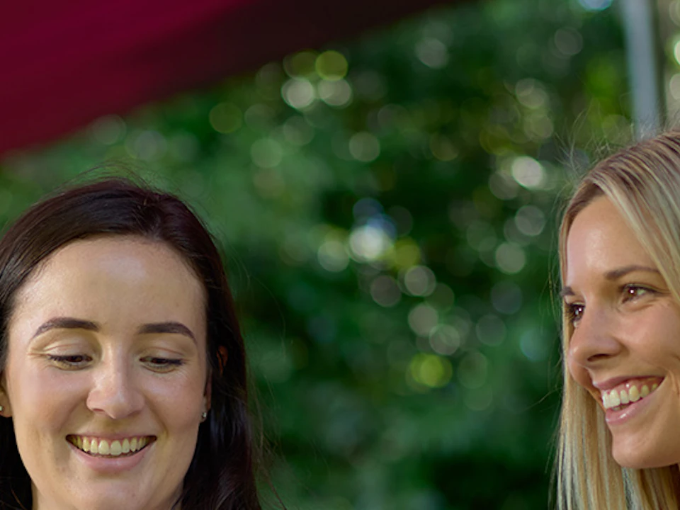 Three people smiling and holding ice cream in waffle cones, standing outdoors under a maroon canopy near large green fruits.