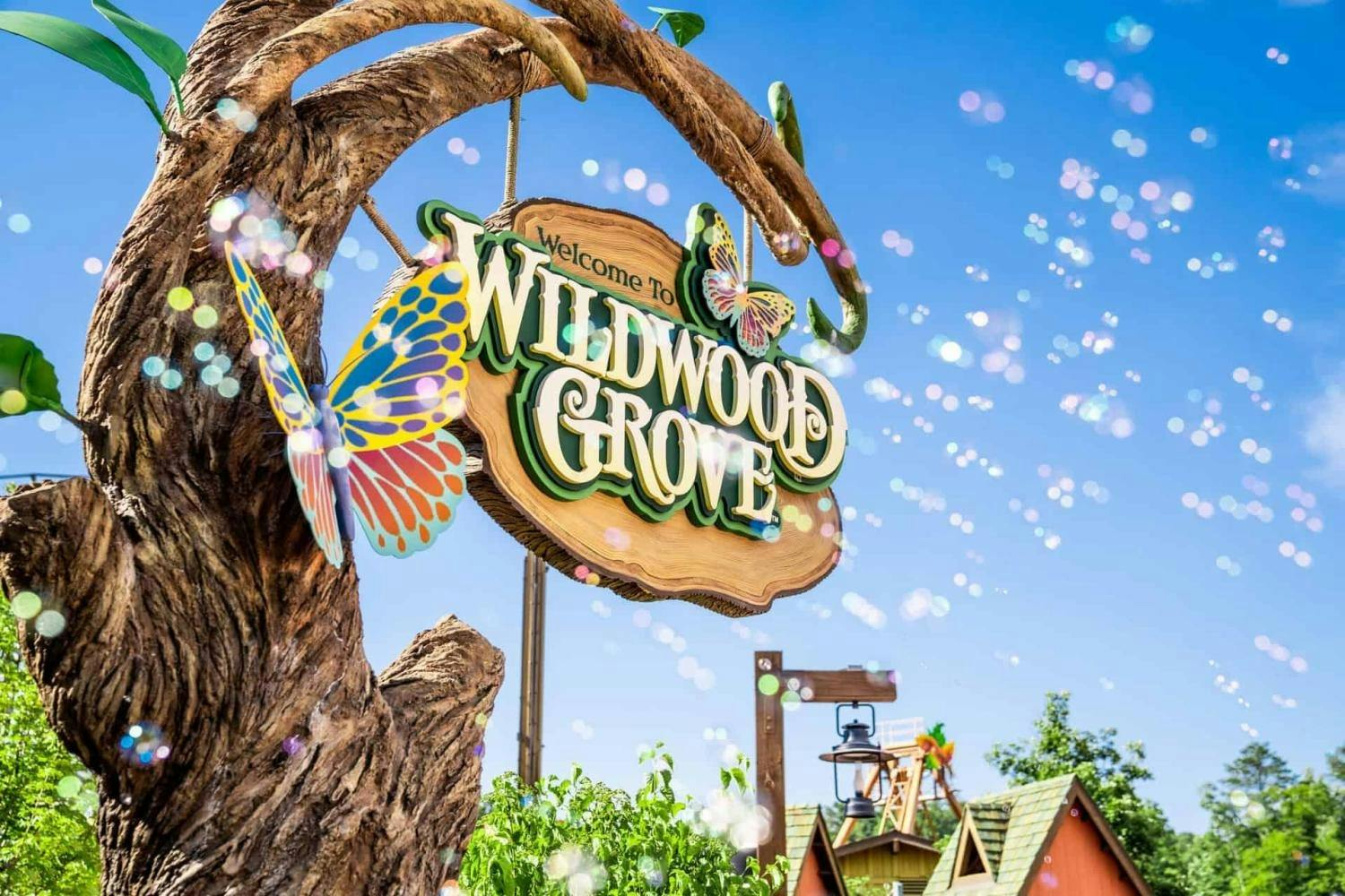 A colorful wooden sign reading 'Welcome to Wildwood Grove' hangs on a tree, surrounded by vibrant decorations and bubbles.