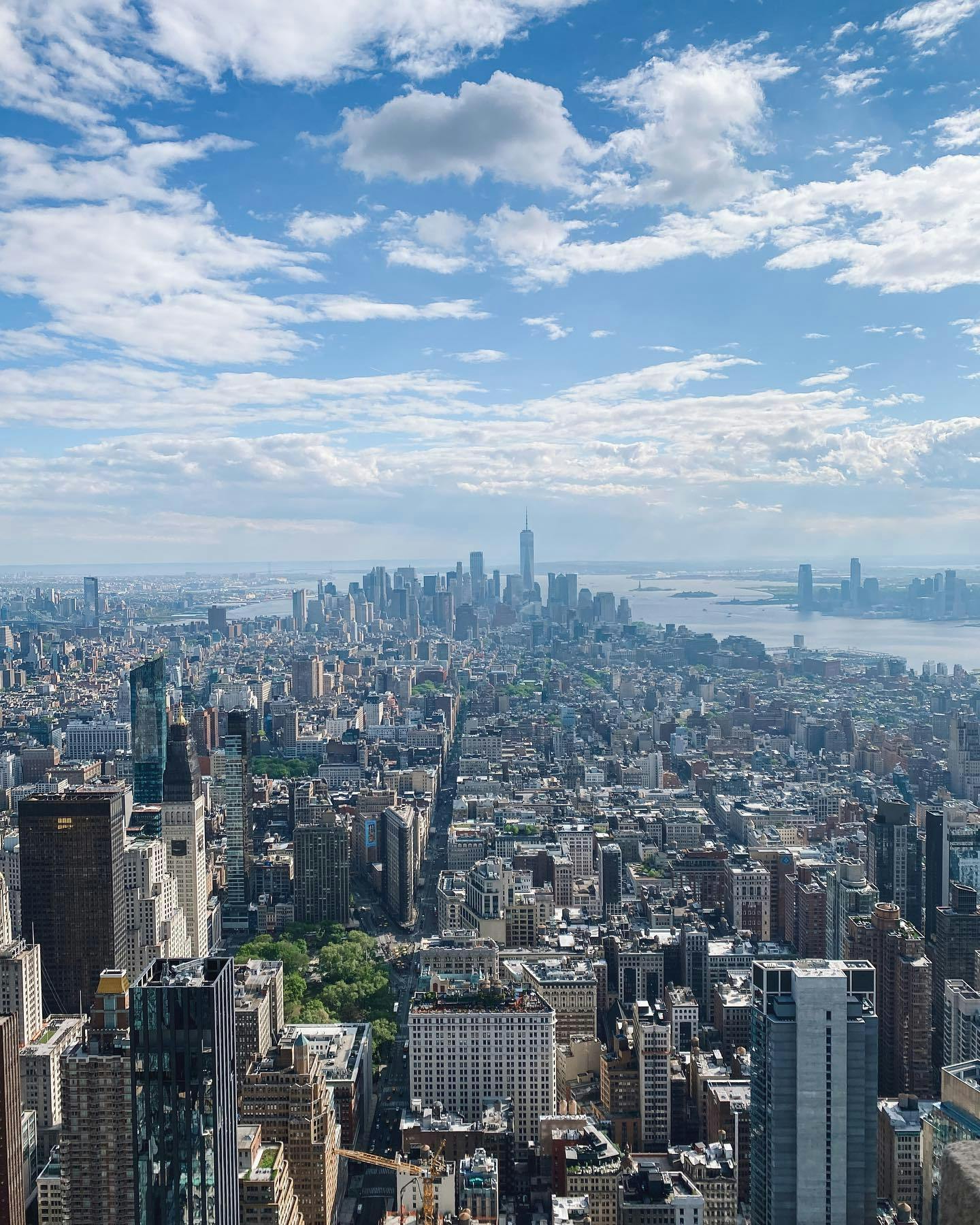 Vista aèria d'un paisatge urbà amb edificis alts, un horitzó llunyà i un riu sota un cel parcialment ennuvolat.