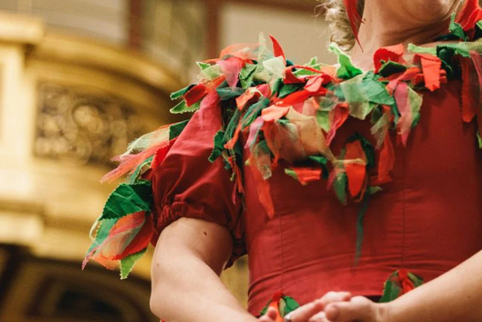 A woman in a red dress adorned with green and red leaves smiling in an ornate, gilded building interior.
