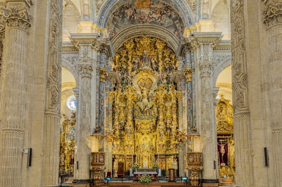 An ornate church interior with an intricately detailed gilded altar and arched ceilings decorated with frescoes.