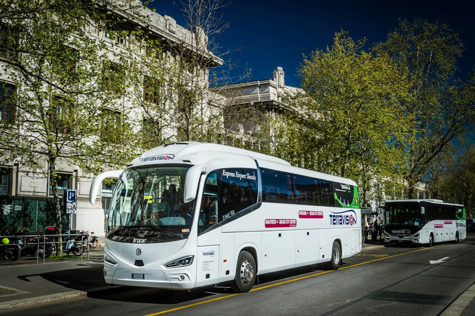 A white tour bus with "Terravision" branding parked on a city street, with buildings and trees in the background.