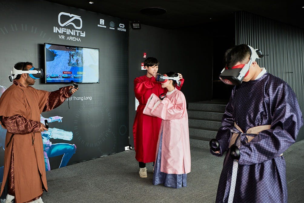 A group of people wearing VR headsets and traditional Korean attire interact in a room labeled "Infinity VR Arena."