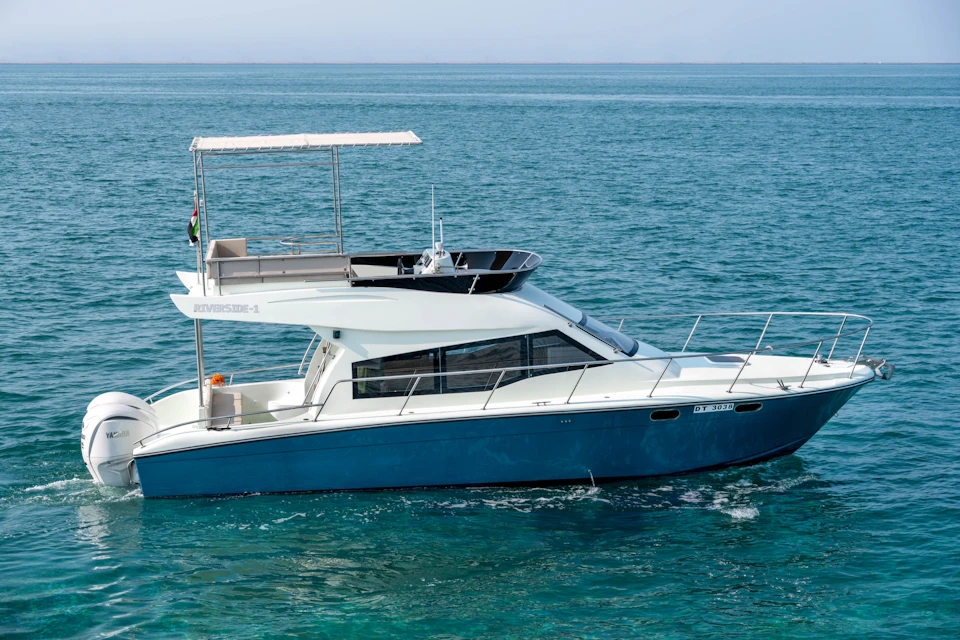 A small motorboat with a blue hull and white cabin, featuring an upper deck canopy, floating on calm, clear ocean water.