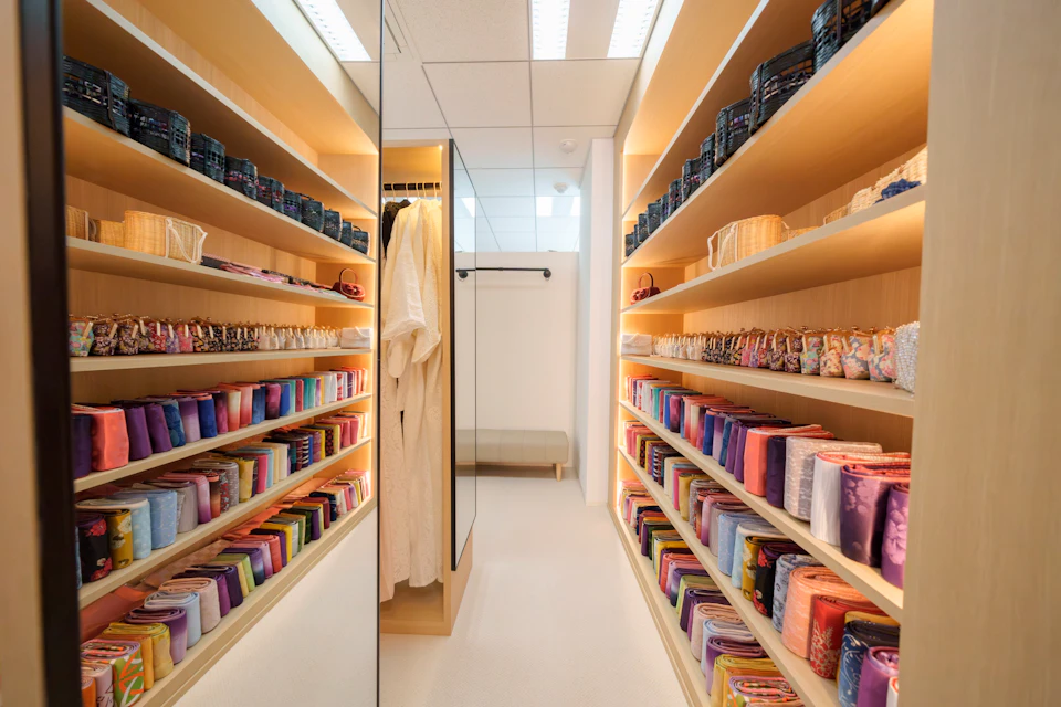 A well-organized room with shelves holding colorful fabric rolls and a hanging white garment, illuminated by ceiling lights.
