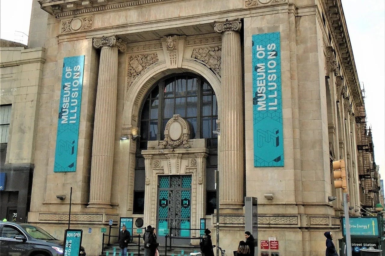 Fachada do Museu das Ilusões com uma grande entrada em arco e cartazes publicitários do museu.
