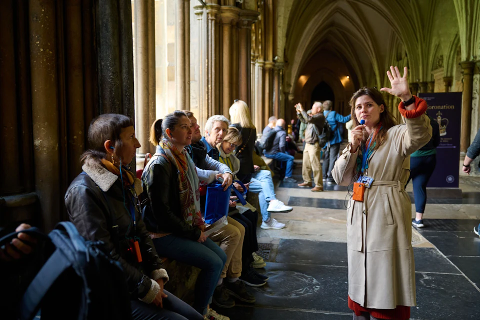 A tour guide speaking to a seated group in a historic building with vaulted ceilings and Gothic architecture.