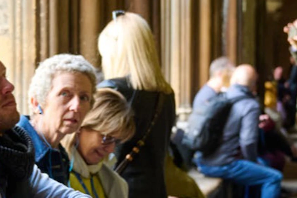 A tour guide speaking to a seated group in a historic building with vaulted ceilings and Gothic architecture.