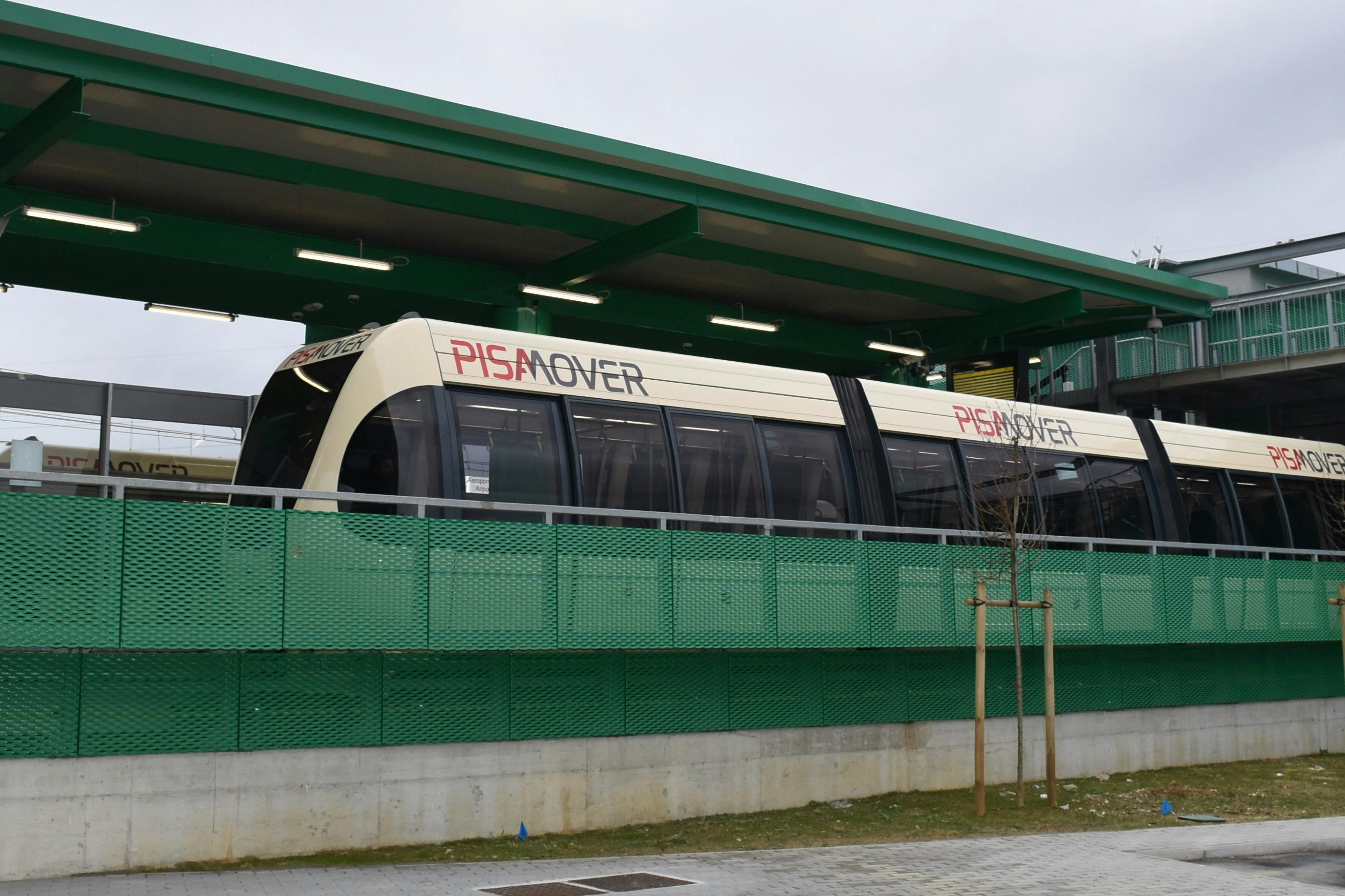 在阴天，一辆PisaMover电车会在一个现代化的绿色车站站台停靠。