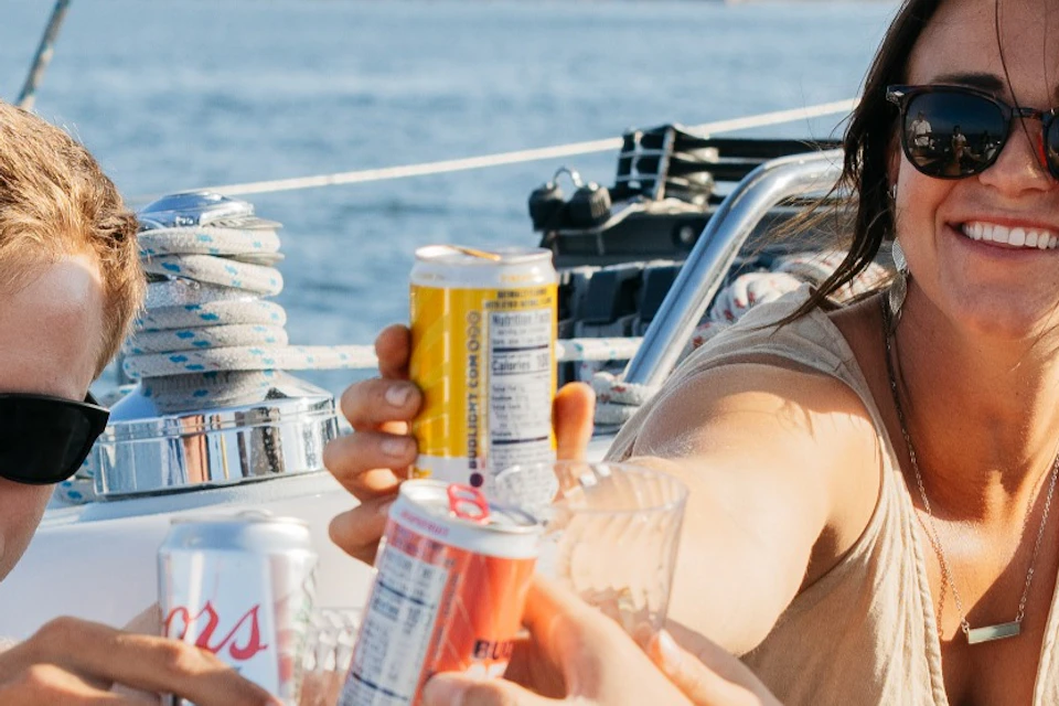 Group of young adults sitting in the cockpit of a sailboat toasting drinks with Point Loma in the background