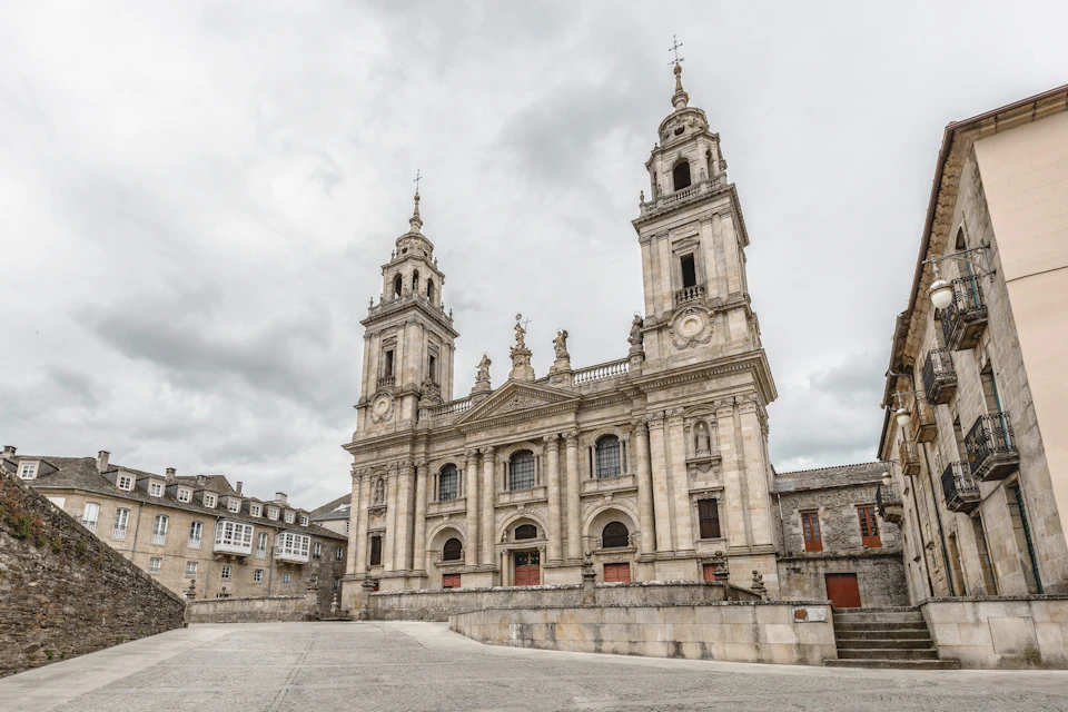 A large, ornate, historic stone cathedral with two tall towers and statues, set against a cloudy sky.