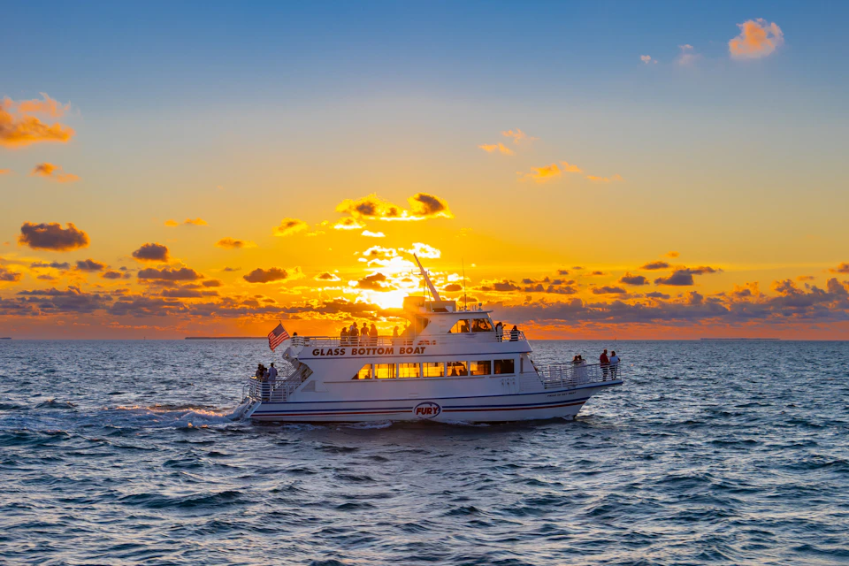 A glass-bottom boat on the ocean at sunset with the sun illuminating the sky and clouds.