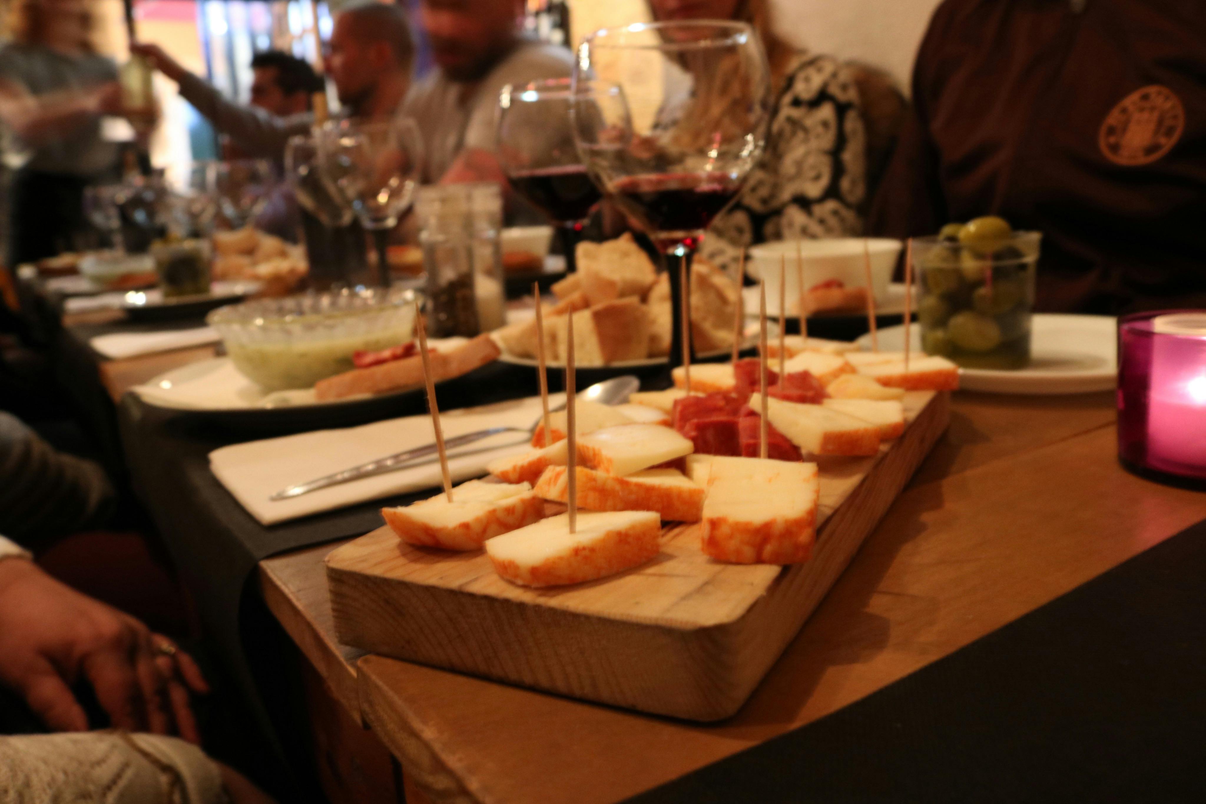 Tagliere di tapas con formaggio, pane e vino in un ambiente vivace
