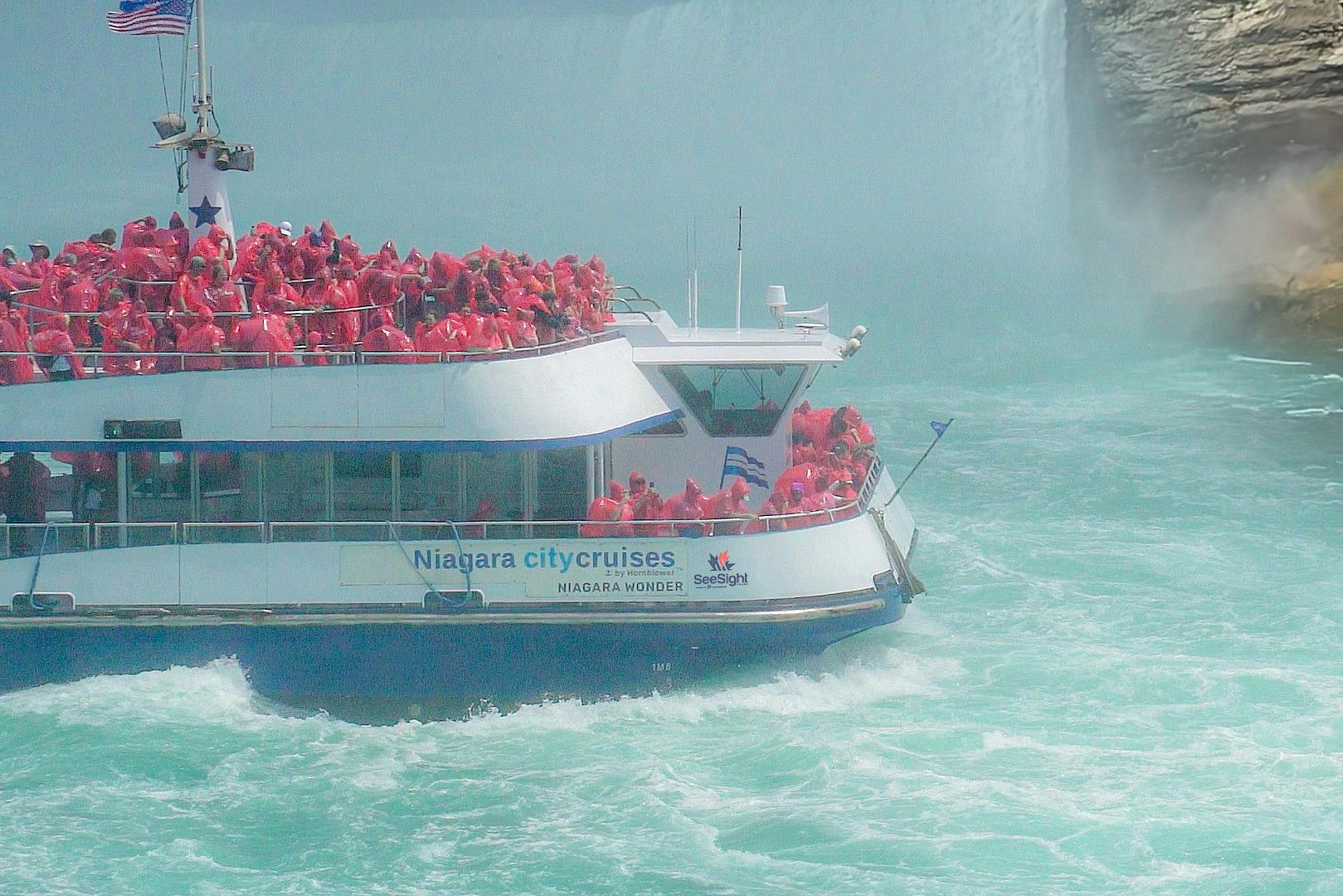 赤いポンチョを着た人でいっぱいのボートが「ナイアガラシティクルーズ」と書かれたナイアガラフォールズに近づいています。