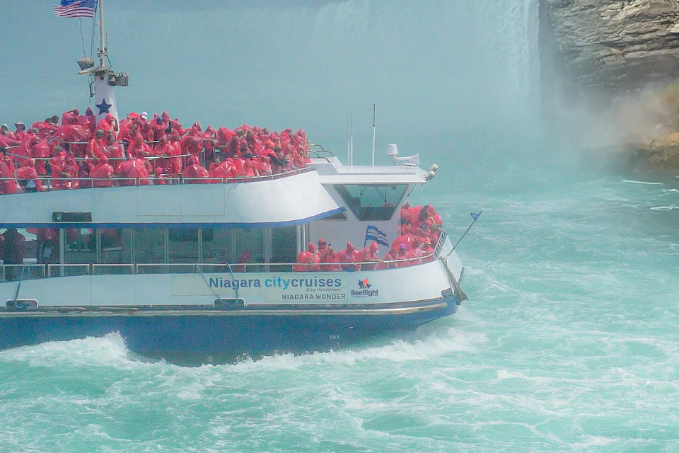 A boat filled with people wearing red ponchos approaches Niagara Falls, labeled "Niagara City Cruises."