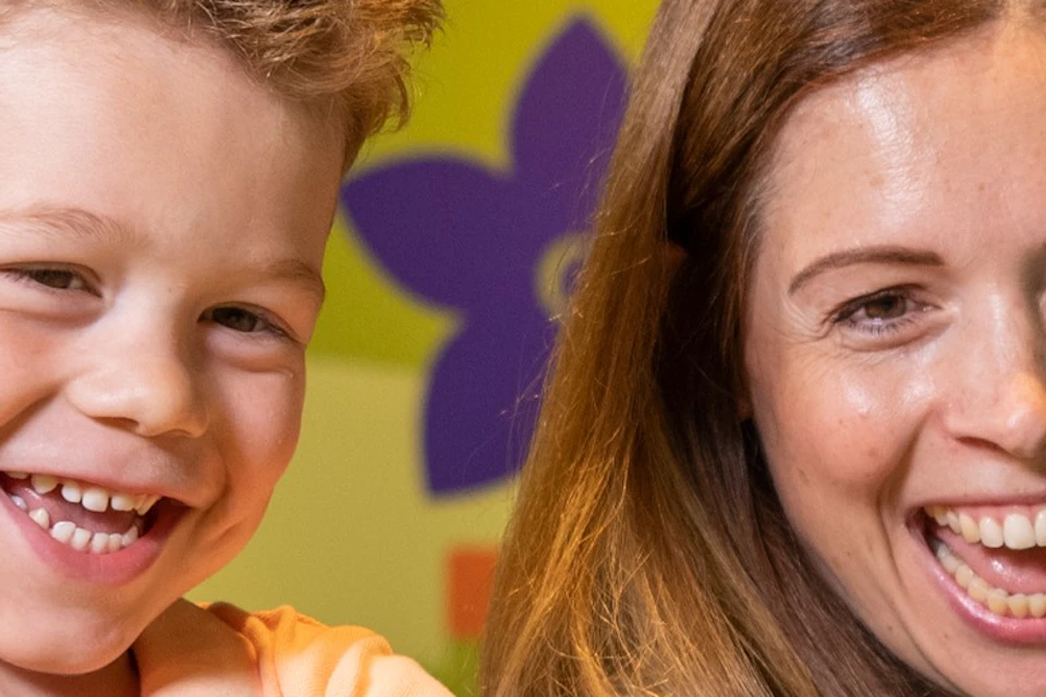 A smiling woman and child playing a fishing game indoors with colorful background. The child is holding the fishing rod.