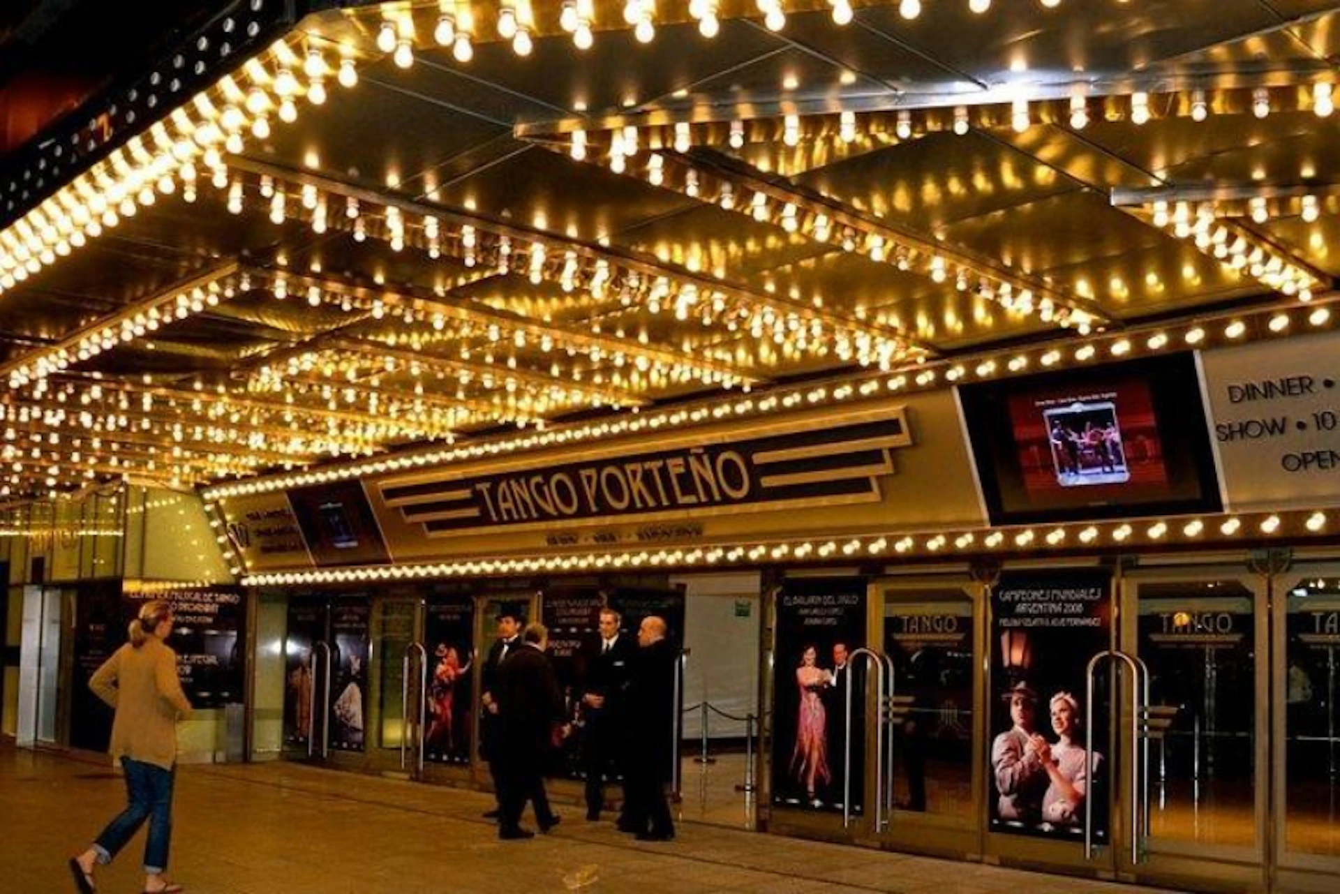 Illuminated theater entrance with "Tango Porteño" signage, posters of dancers, and people in formal attire standing outside.