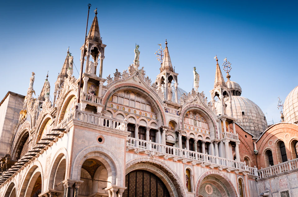 Facade of a historic building with intricate arches, statues, and spires, against a clear blue sky.