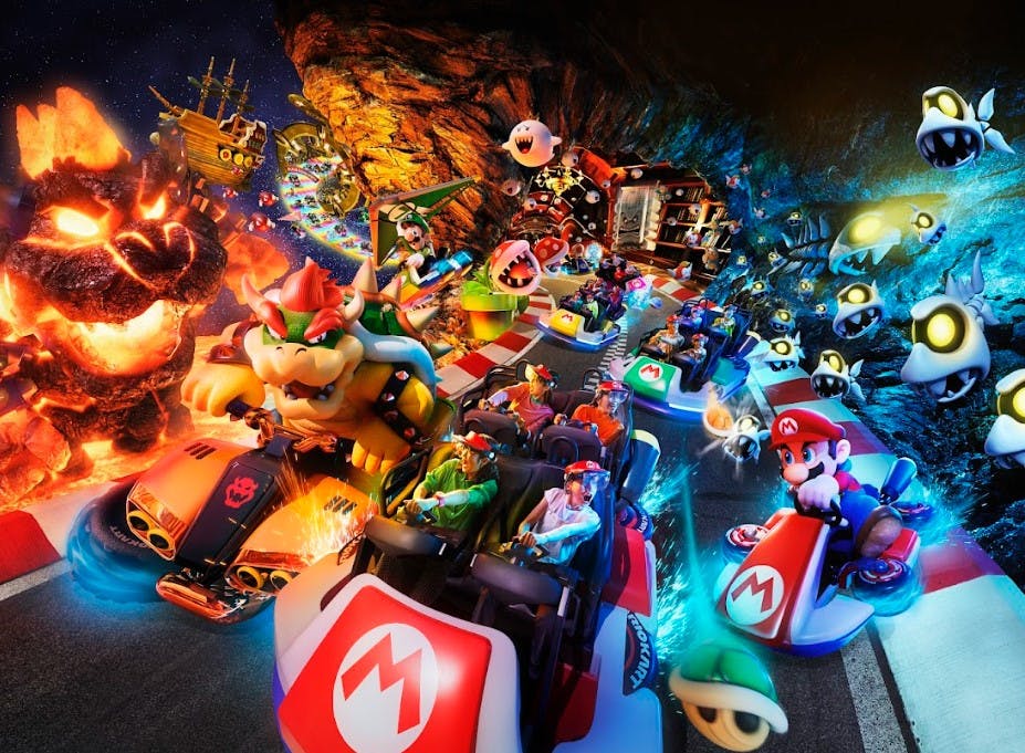Živá scéna s postavami Mario Kart závodícími v motokárách na trati obklopené animovanými prvky, plameny a barevnými světly.