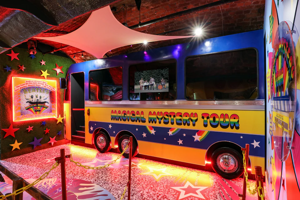A colorful bus with "Magical Mystery Tour" written on the side, displayed in a vibrant, starry indoor setting.