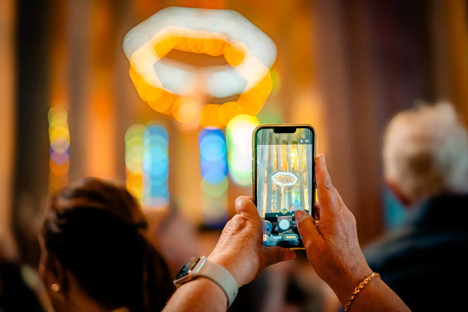 A person holds a smartphone taking a photo of colorful lights inside a building with stained glass windows.