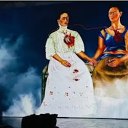 Två kvinnor sitter och håller varandra i handen, var och en med ett synligt hjärta sammankopplat med ett blodkärl, mot en grumlig blå bakgrund.