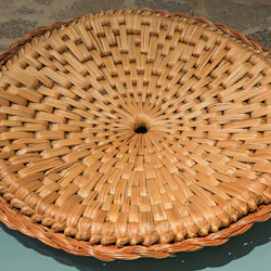 En rund korg med ett centralt hål, vävd i ett spiralmönster, placerad på ett stengolv.