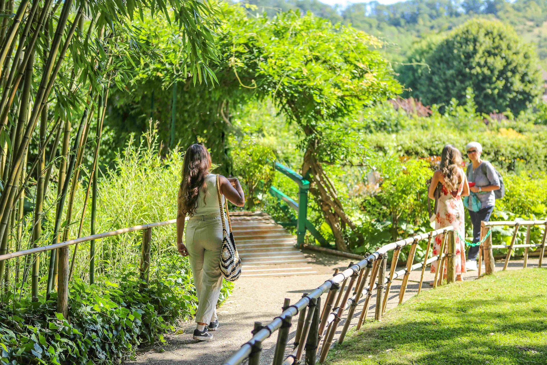 Two women walking on a garden path covered with greenery, one in the foreground and one in the distance.