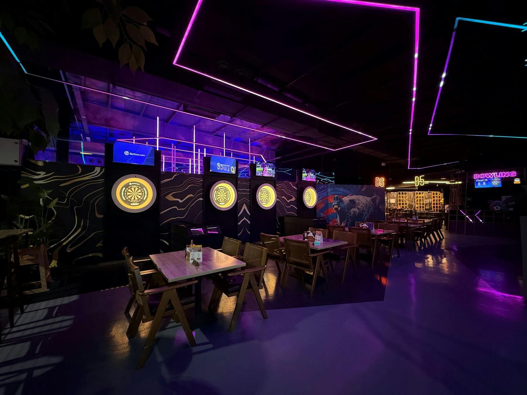 Μια σύγχρονη εσωτερική στοά με βελάκια με λαμπερά βελάκια, τραπέζια με καρέκλες και ζωντανό φωτισμό νέον στην οροφή.