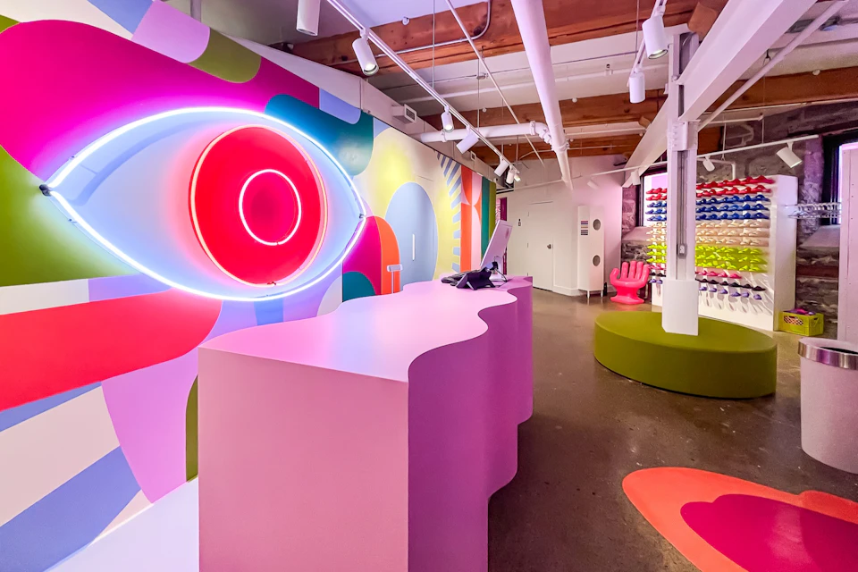 Brightly colored interior with pink wavy desk, neon eye design, and vibrant decor, featuring modern furniture and displays.