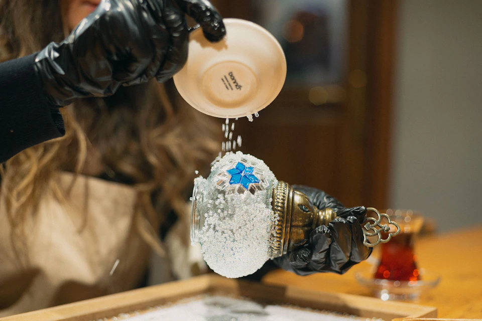 Participant pouring small white stones onto a mosaic lamp being crafted.