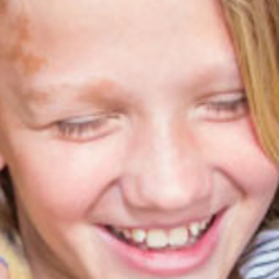 A smiling girl in a striped shirt holds a small, furry animal on her shoulder inside a green-painted enclosure.