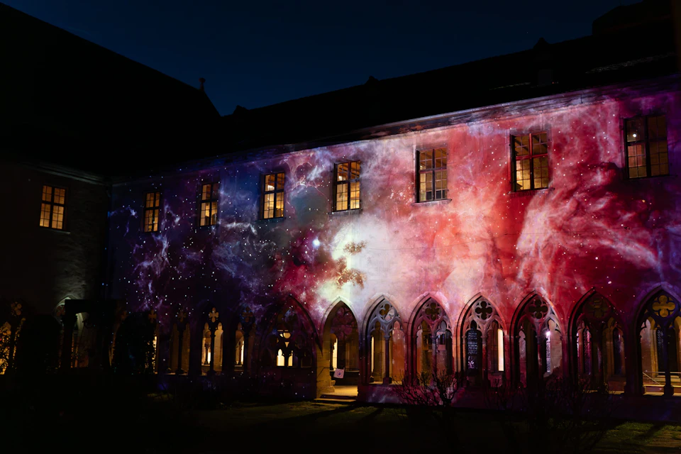 A building with arched windows illuminated by a vibrant cosmic projection at night.