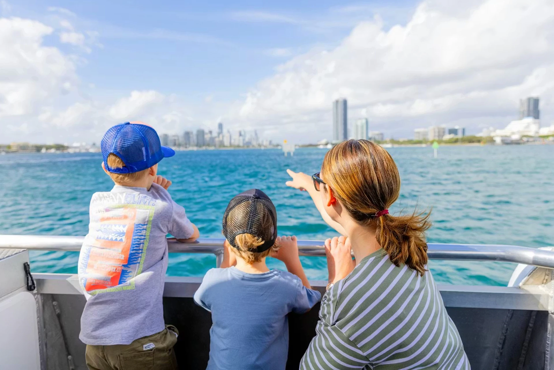 Three people, including two children, on a boat looking at a city skyline across a body of water on a sunny day.