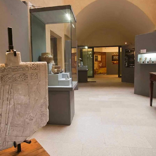 A museum exhibit featuring stone carvings and artifacts displayed in glass cases within a room with arched ceilings.