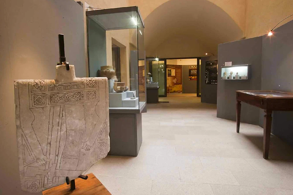 A museum exhibit featuring stone carvings and artifacts displayed in glass cases within a room with arched ceilings.