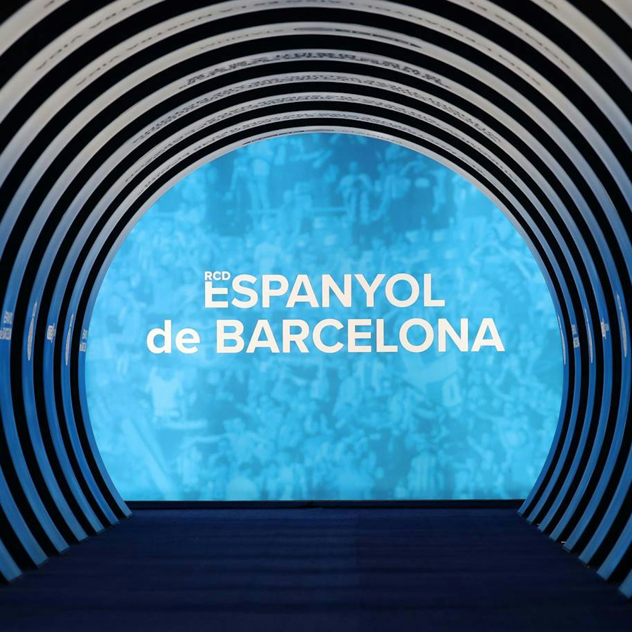 Böjd tunnelstruktur med en upplyst blå ändvägg som visar texten "RCD ESPANYOL de BARCELONA."