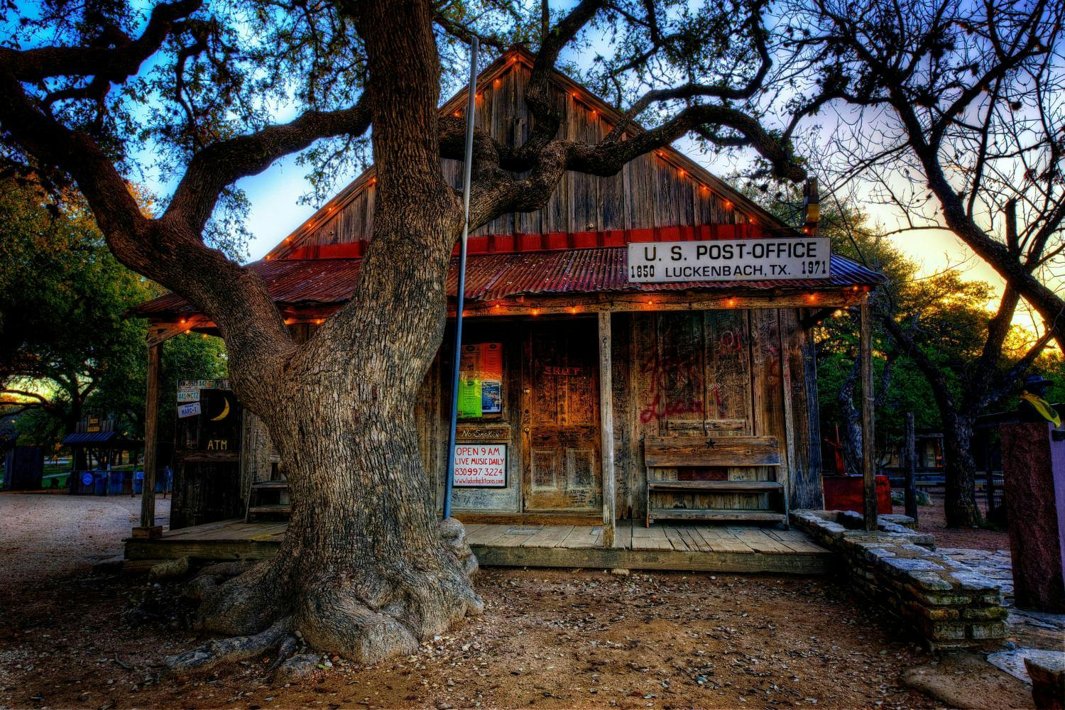 Rustic wooden post office with a large tree in front, located in Luckenbach, Texas. The building has weathered wood and a porch.