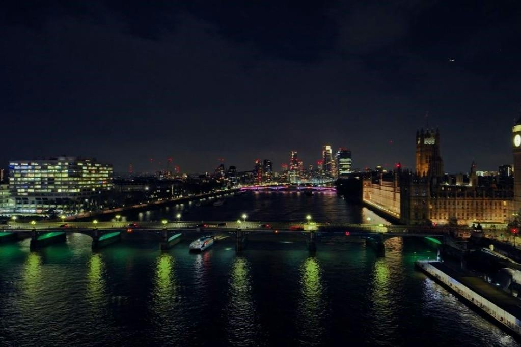 A cityscape at night showing a river, illuminated bridges, and buildings with lit windows and lights in the distance.
