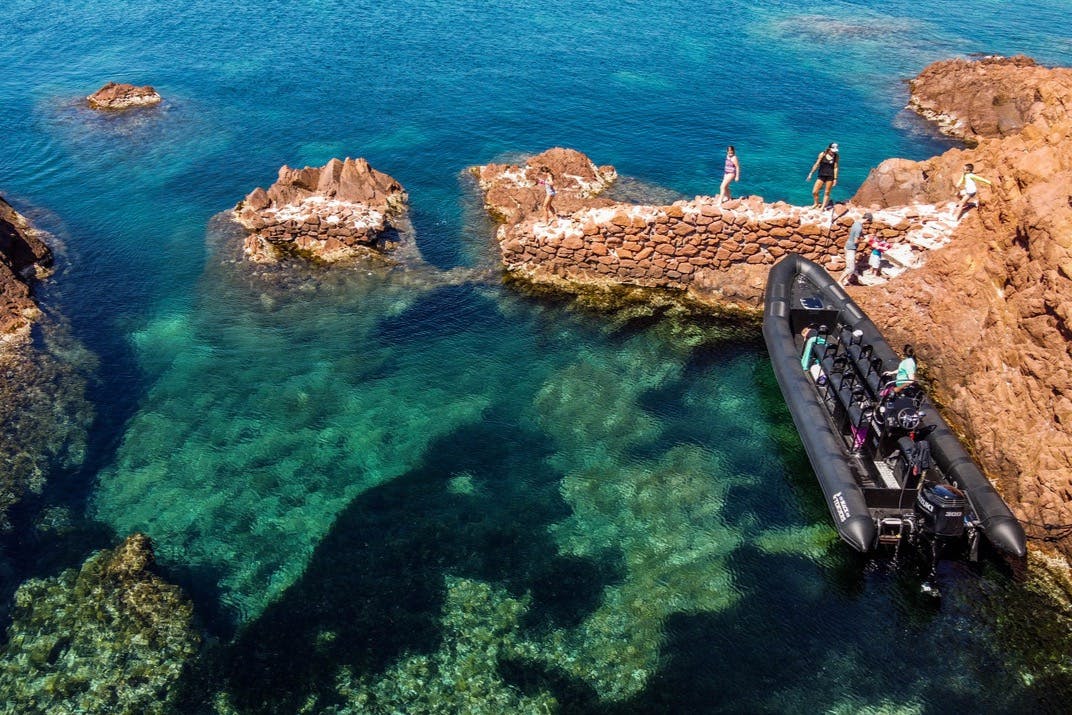 人们站在清澈的蓝色海水旁的岩石码头上，附近停着一艘橡皮艇。