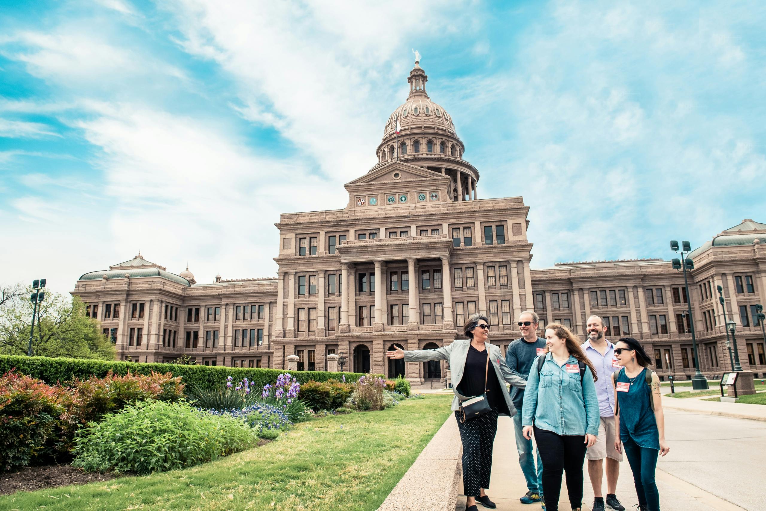 Un groupe de personnes marchant et discutant devant un grand bâtiment avec un dôme sous un ciel bleu.