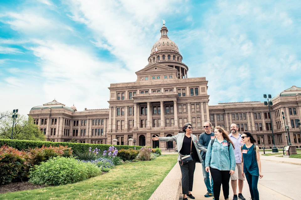 A group of six people standing in front of a large historic building under a partly cloudy blue sky.