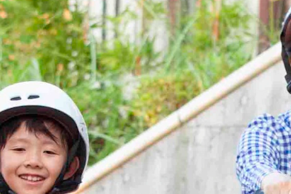Three people wearing helmets are seated in colorful go-karts, ready to ride on a paved track outdoors.