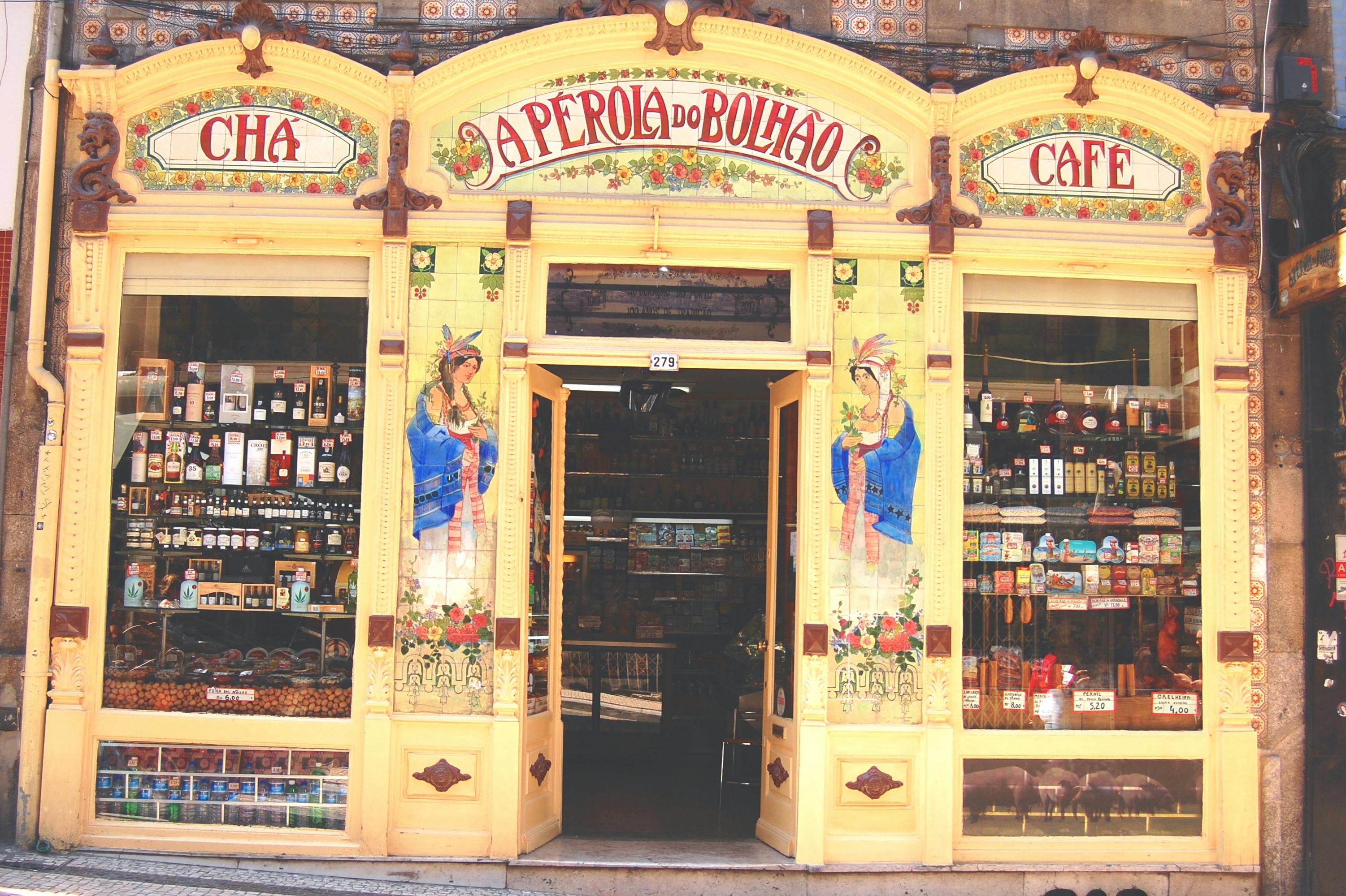 Κίτρινη βιτρίνα του "A Perola do Bolhao" με διακοσμητικές τοιχογραφίες και ράφια εφοδιασμένα με διάφορα αγαθά στο εσωτερικό.